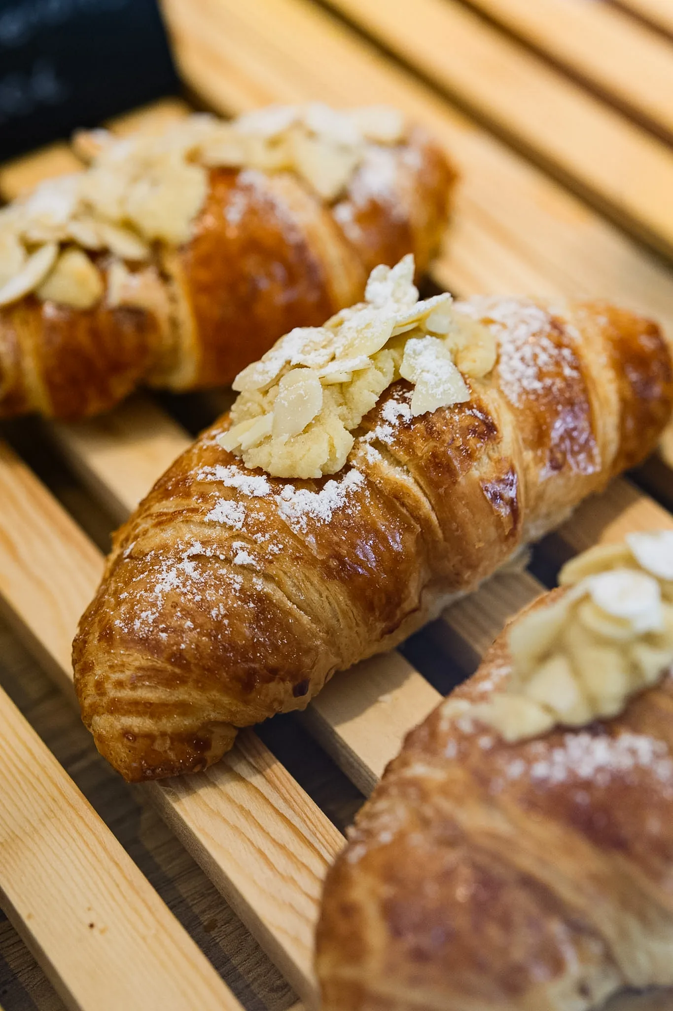 Almond croissants freshly finished with sliced almonds and powdered sugar.