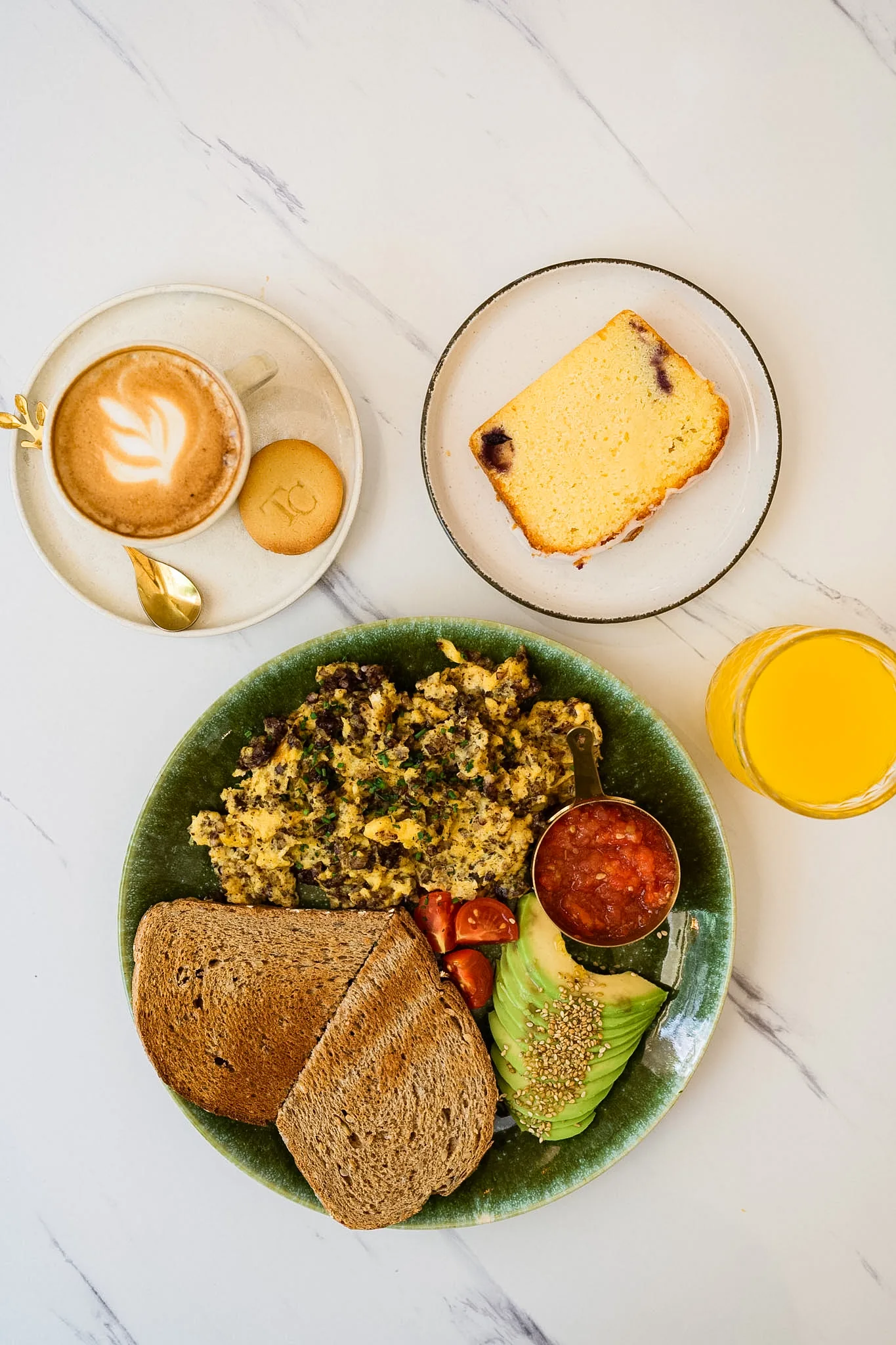 A complete brunch with eggs, avocado, toast, coffee, juice and cake.