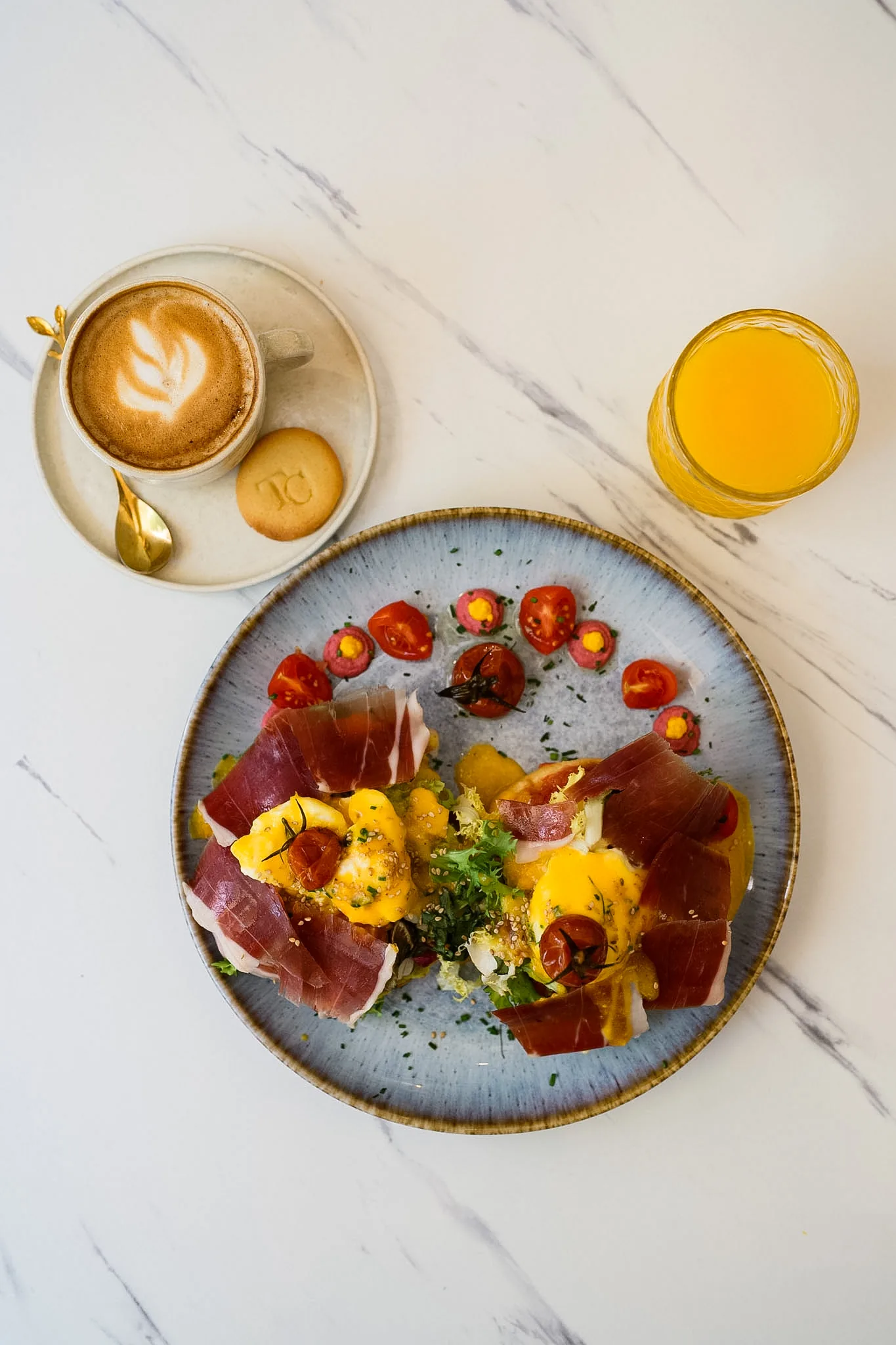 A composed brunch plate with coffee and fresh orange juice on pale marble.