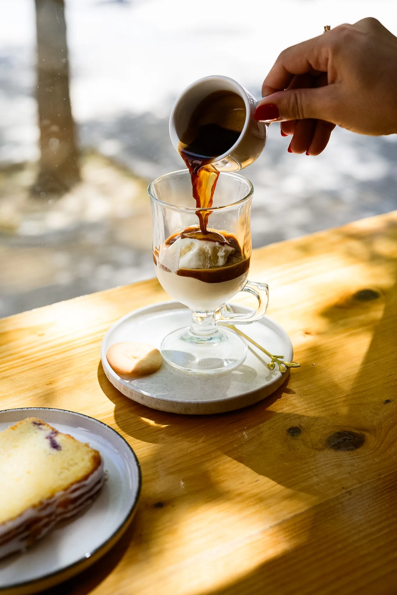 Fresh espresso being poured over ice at a sunlit table.