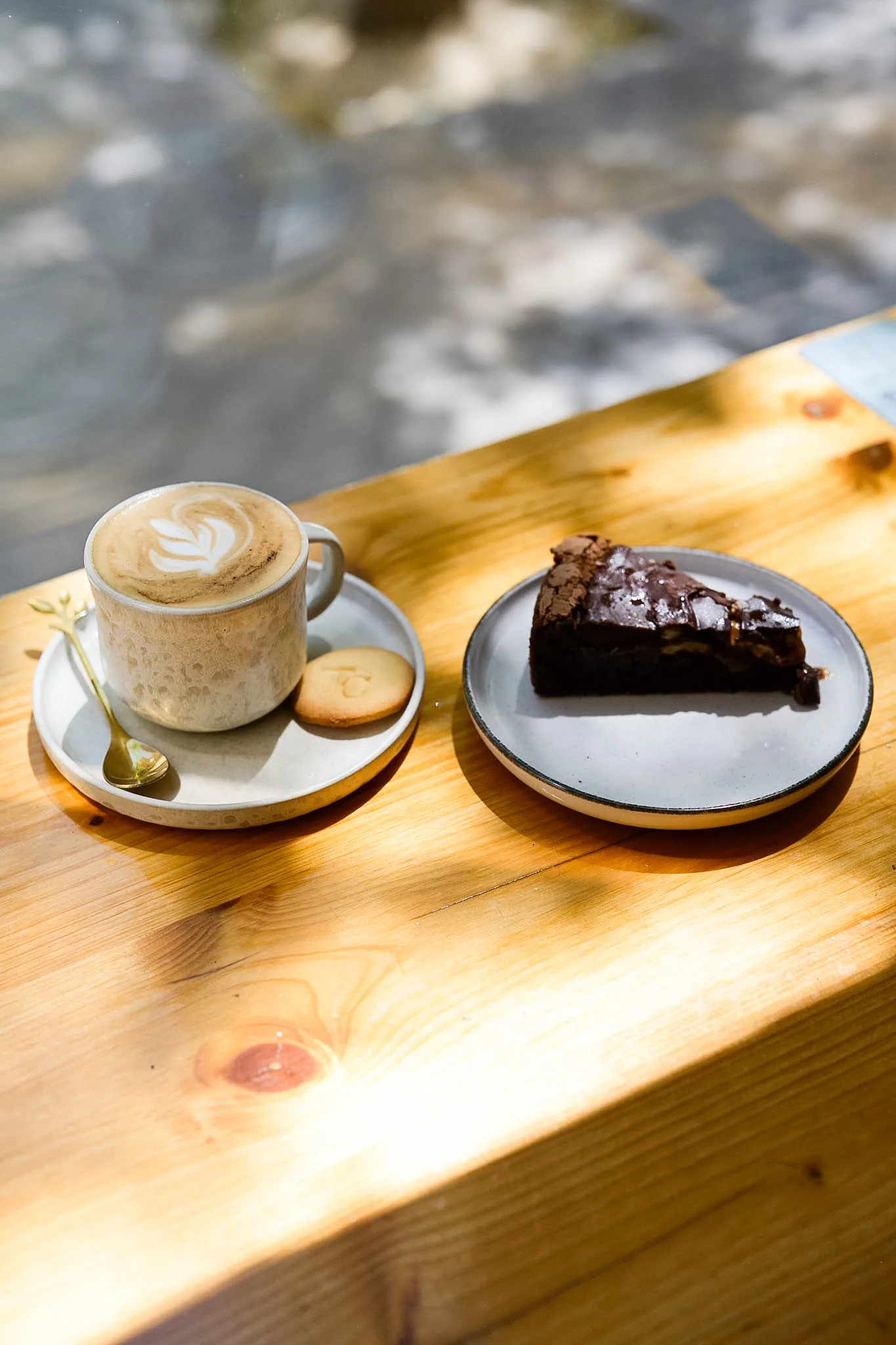 A latte and a slice of chocolate cake in warm window light.