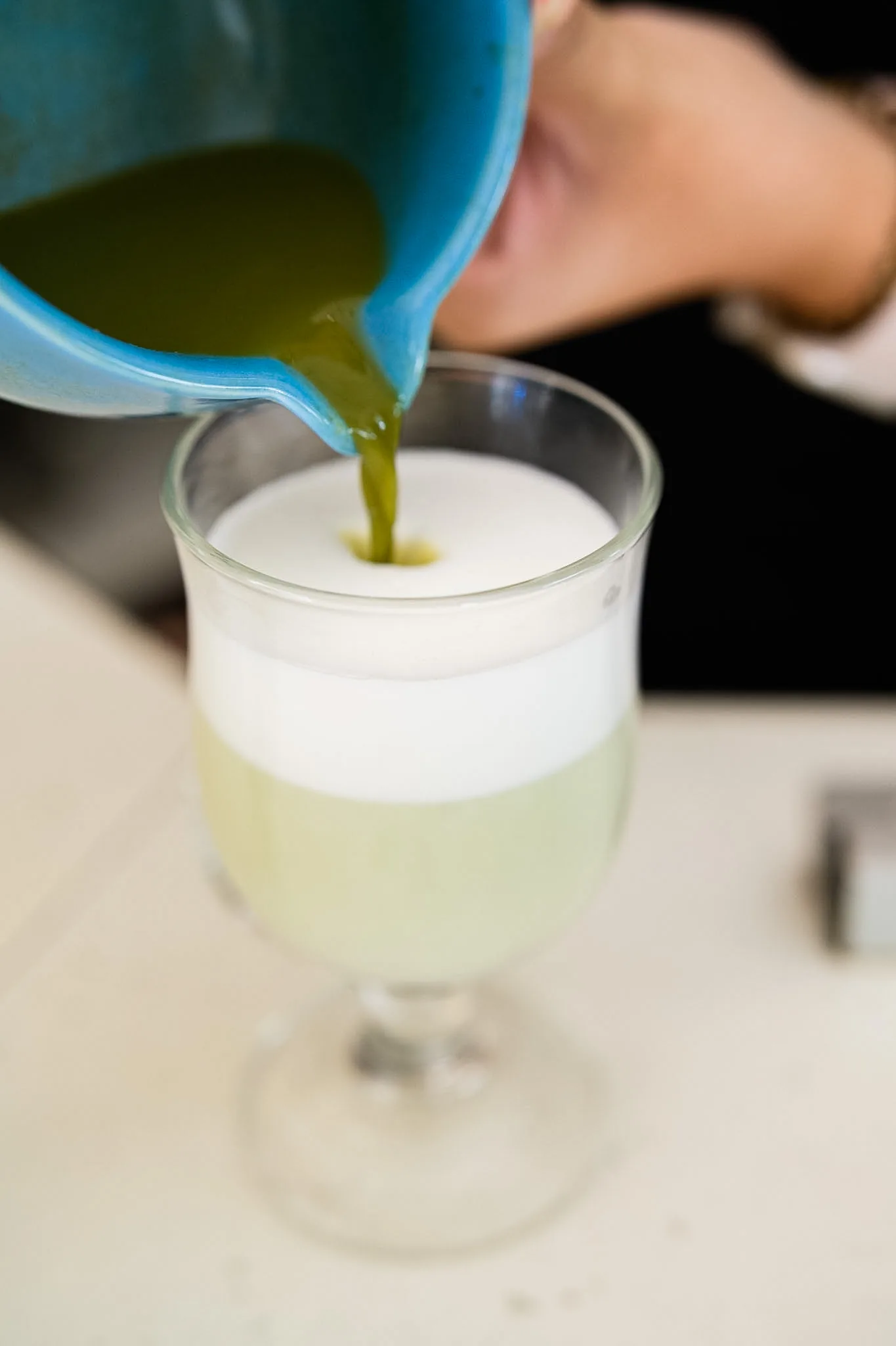 Matcha being poured over milk to finish a chilled drink.