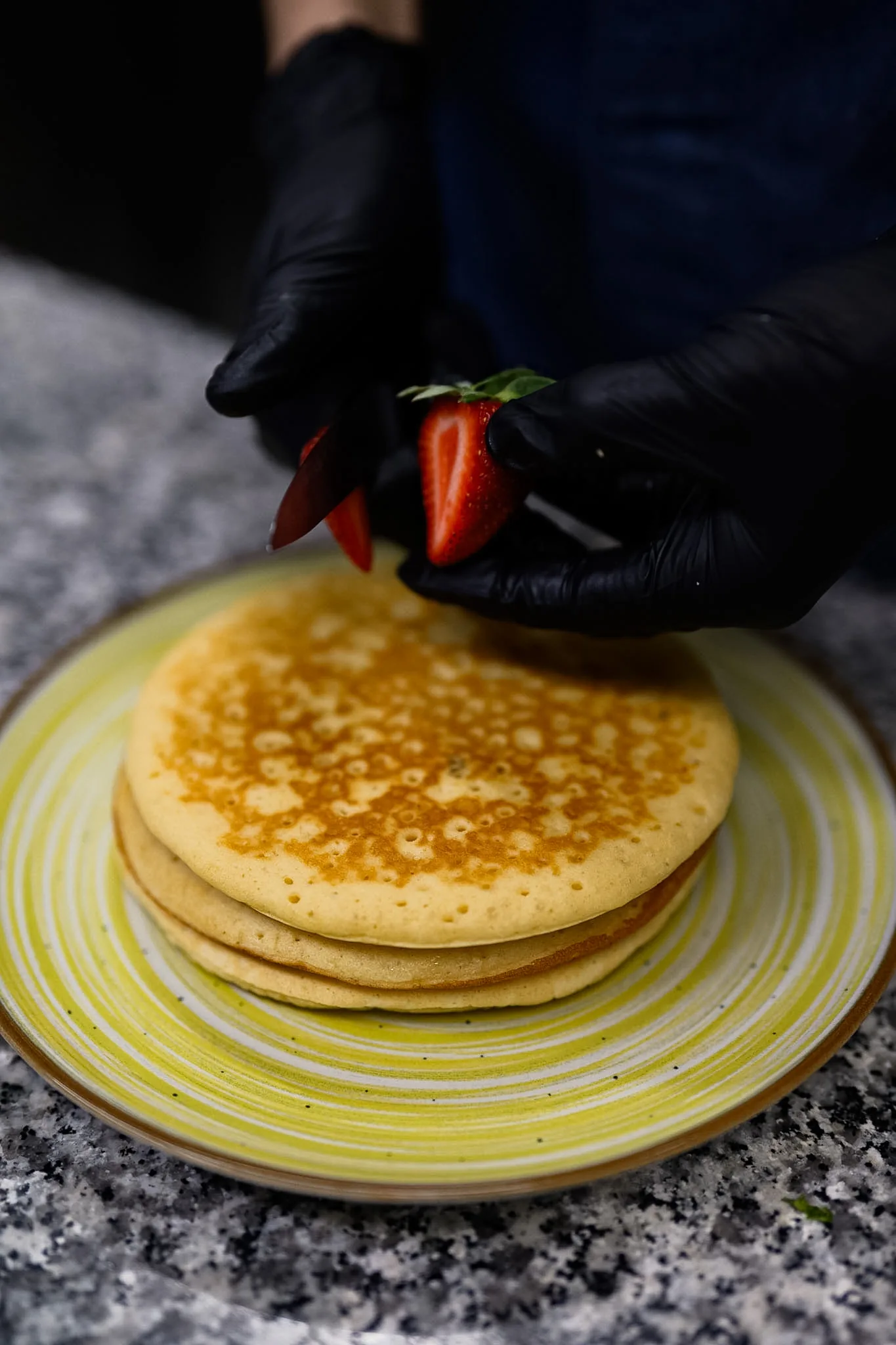 A strawberry being placed onto freshly prepared pancakes.