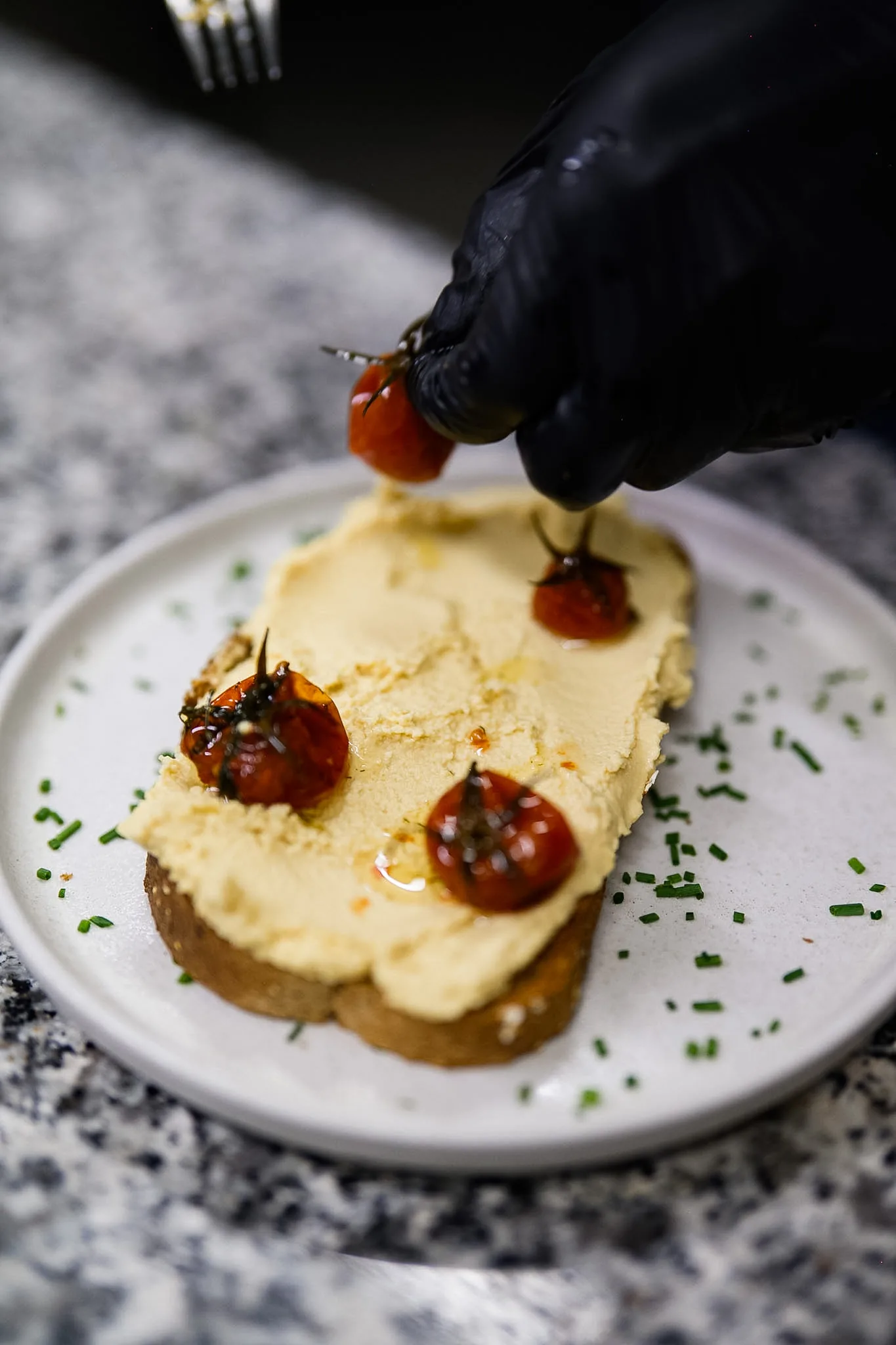 Roasted tomatoes being added to a freshly prepared toast.