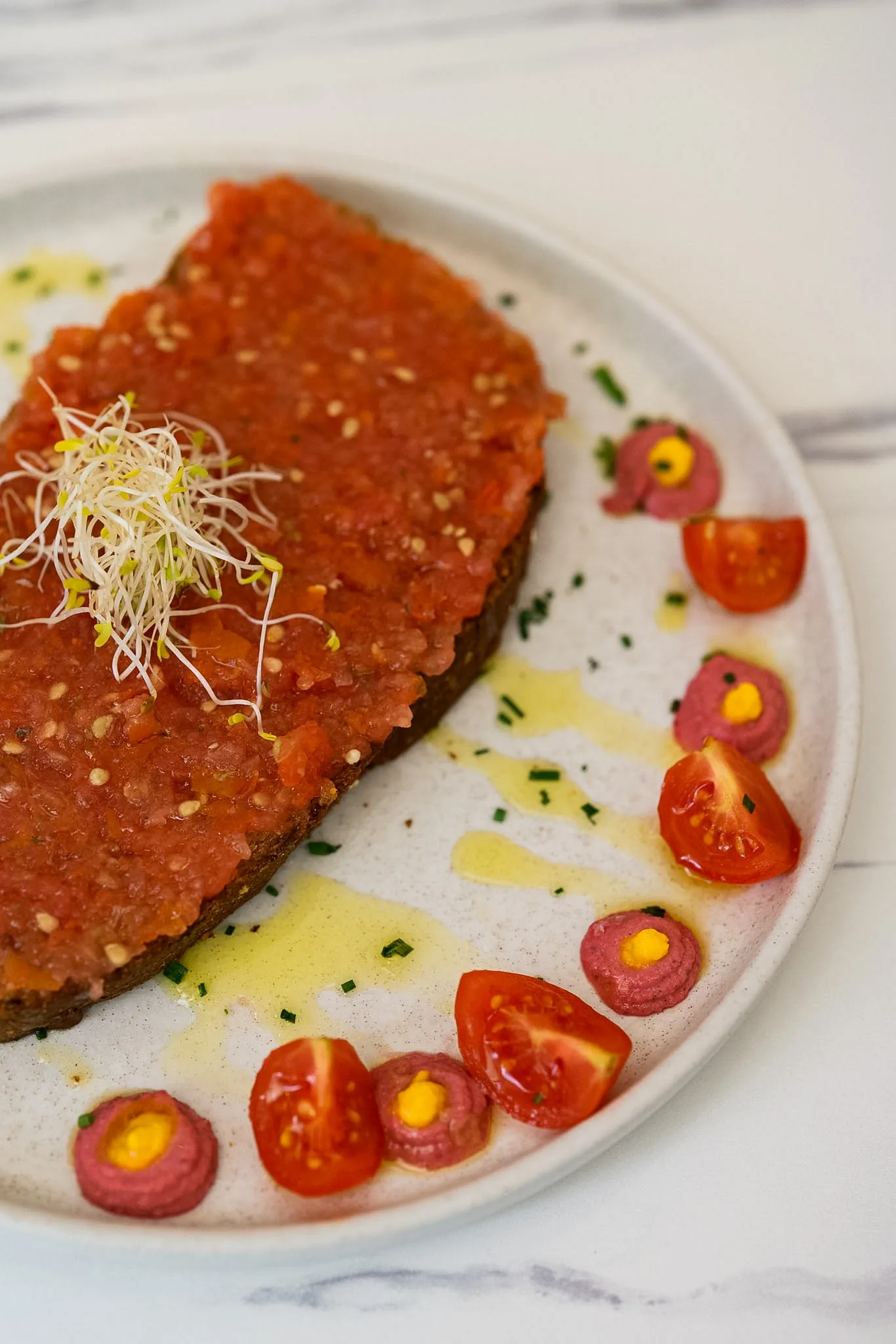 Tomato toast with sprouts and cherry tomatoes on pale marble.
